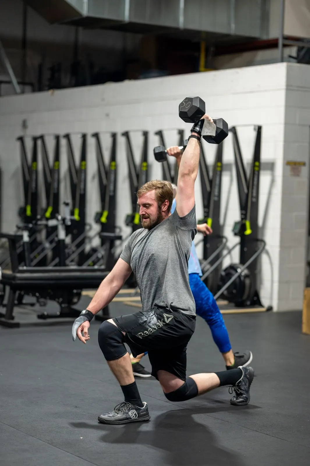 A member in a deep lunge holding a dumbbell overhead
