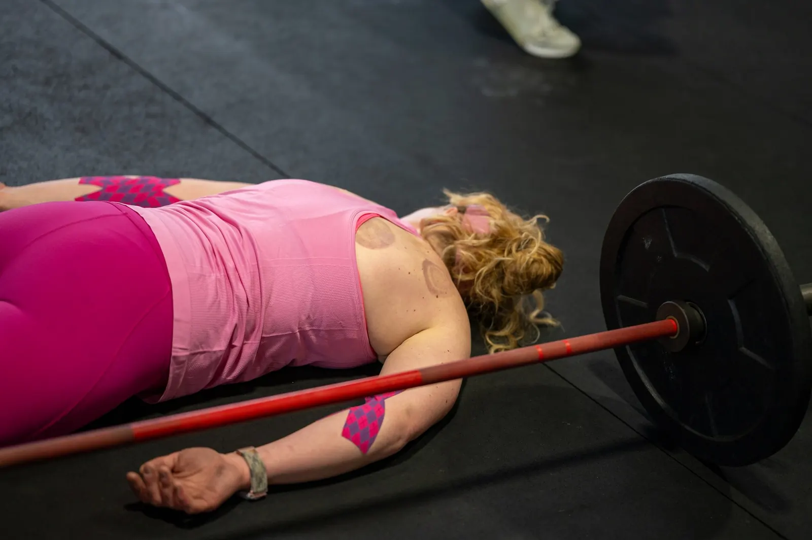 A member lying on the floor beside her barbell after the workout
