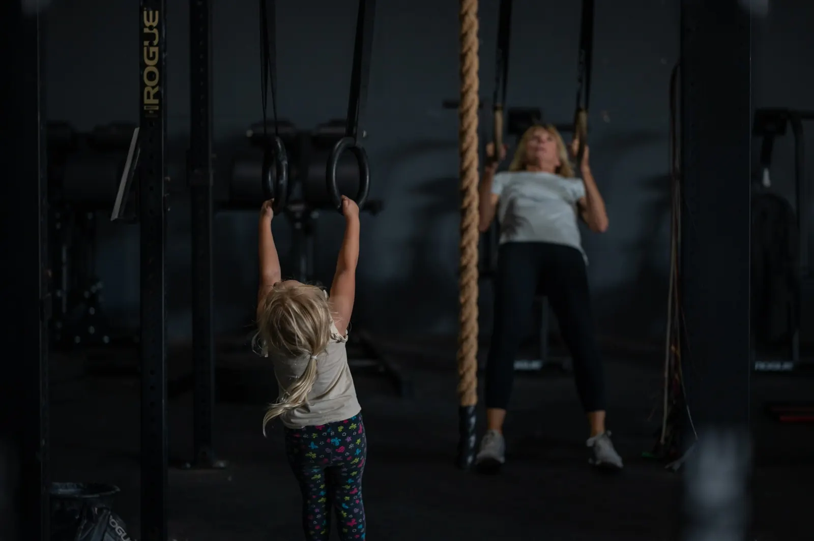 A young athlete hanging from the rig while a member trains beside her