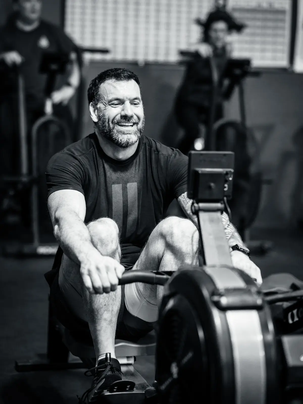 A member smiling on the rower while the class works behind him