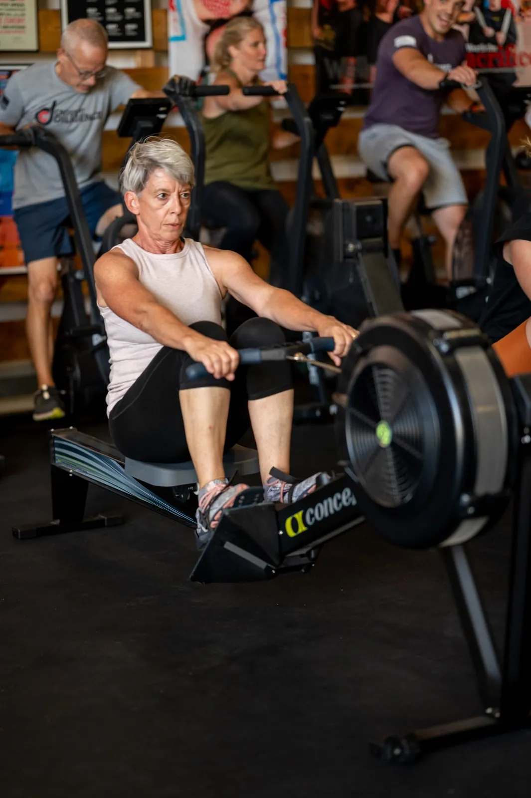 A member rowing on a Concept2 rower with a row of bikes behind her