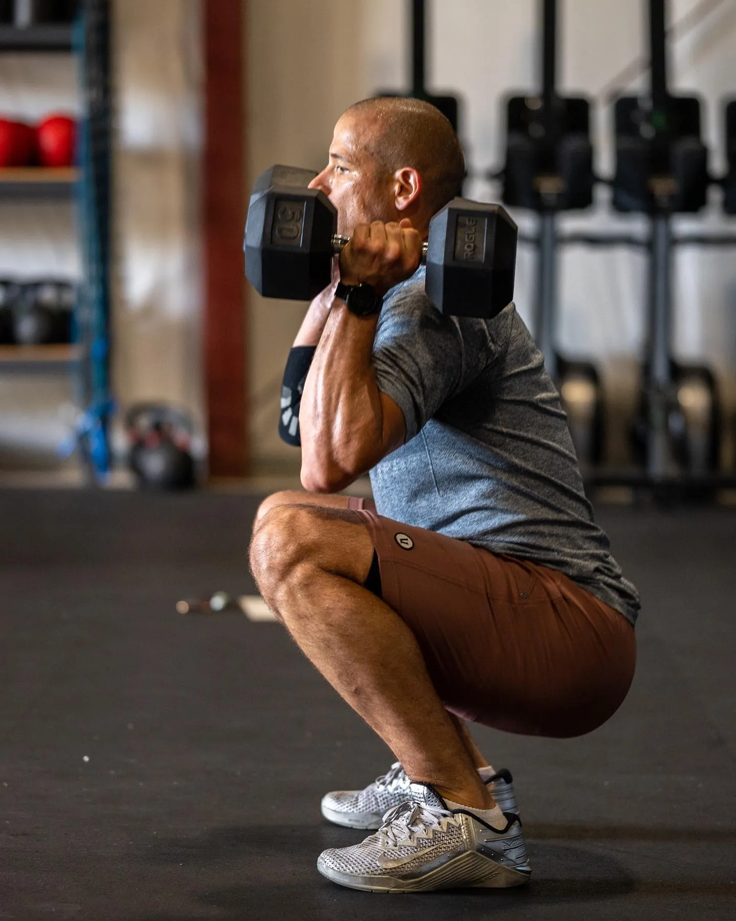 A member squatting with dumbbells on his shoulders
