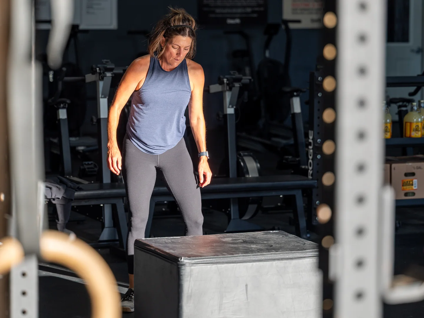 A member stepping up to a plyo box, framed by the gymnastics rings